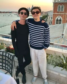 two men standing next to each other on top of a roof near the water and buildings