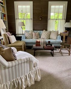 a living room filled with lots of furniture and bookshelves next to two windows