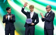 three men in tuxedos applauding on stage