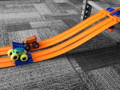 an orange toy track with monster trucks on it in the middle of a carpeted area