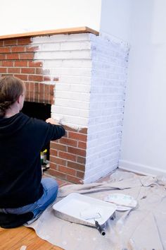 a woman sitting on the floor painting a brick fireplace