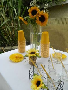 sunflowers are arranged in vases on a table with glasses and straws