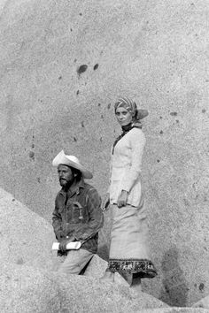 black and white photograph of two people standing next to each other in front of a stone wall