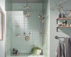 a bathroom with green tile and white fixtures, including a shower head, hand held faucet, soap dispenser, and shelves