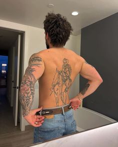 a man with tattoos on his back is standing in front of a mirror and looking at himself