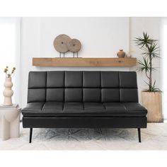 a black leather futon sofa sitting in front of a wall with potted plants