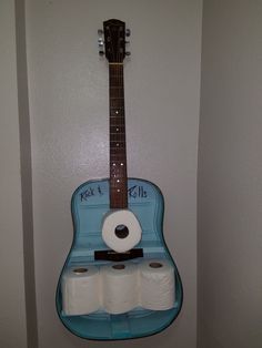 a blue guitar hanging on the wall with toilet paper and roll holders attached to it