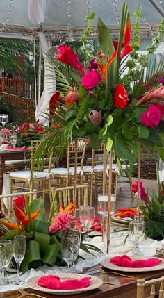 the table is set with pink and red flowers, greenery, and gold place settings