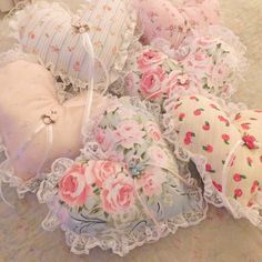 several decorative pillows on a bed with pink flowers and lace trim around the edges, all in pastel colors