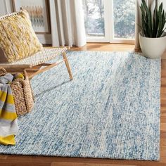 a blue and yellow rug in a living room next to a chair with a potted plant on it