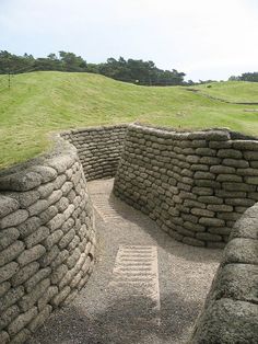 a stone wall with steps leading up to it in the middle of a grassy field