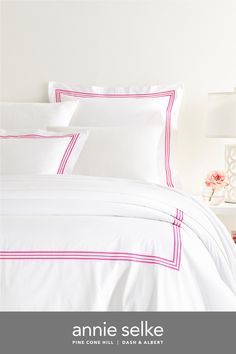 a bed with white sheets and pink trimmings on the pillowcase is shown