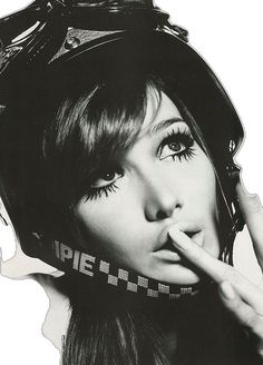 a black and white photo of a woman with her finger in her mouth while wearing a helmet