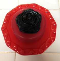 a red plate with a black flower on it sitting on a white tile counter top