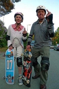 an older man and woman walking down the street with skateboards in their hands, giving the peace sign