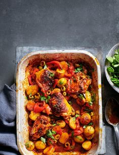 a casserole dish filled with chicken, tomatoes and other veggies on a table