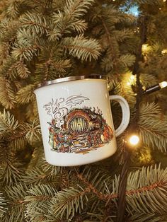 a white coffee cup hanging from the top of a christmas tree with lights on it