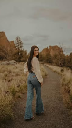 a woman standing in the middle of a dirt road with her back to the camera