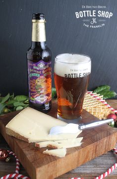 a wooden cutting board topped with cheese next to a beer