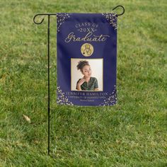 a blue and gold graduation yard flag with a photo on it in the middle of grass