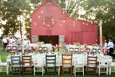 an outdoor table set up in front of a red barn with white chairs and tables