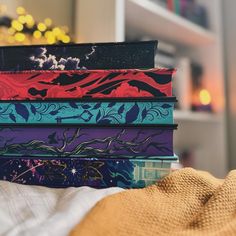 a stack of colorful books sitting on top of a bed next to a pillow and blanket