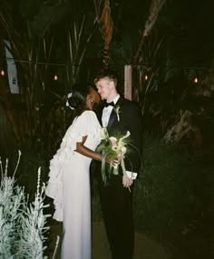 a man and woman standing next to each other in front of some trees at night