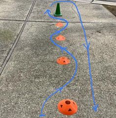 some orange cones are lined up on the sidewalk and one is painted to look like a jack - o'- lantern