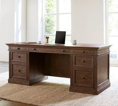 an office desk with two drawers and a laptop on it in front of large windows