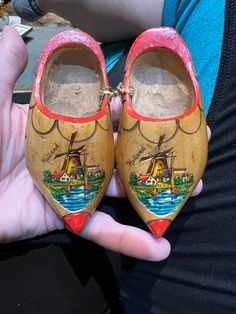 someone is holding two wooden shoes with pictures on the soles and one has a boat painted on it