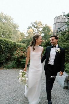 a bride and groom are walking together in the gravel near some bushes on their wedding day