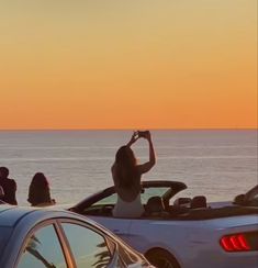 two women are sitting in the back of a convertible car on the beach at sunset