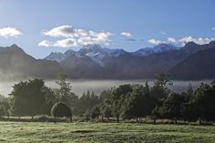 the mountains are covered with mist and clouds in the foreground is a green field