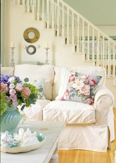 a living room with white furniture and flowers on the coffee table in front of it