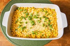 a casserole dish filled with corn and green onions on top of a wooden table