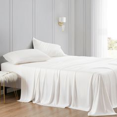 a bed with white sheets and pillows next to a window in a room that has wood floors