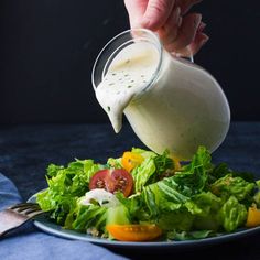 someone pouring dressing into a salad with lettuce and tomatoes