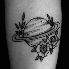 a black and white photo of a saturn tattoo on the right thigh with roses around it