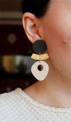 a woman wearing black, white and gold earrings with two circles hanging from the ear