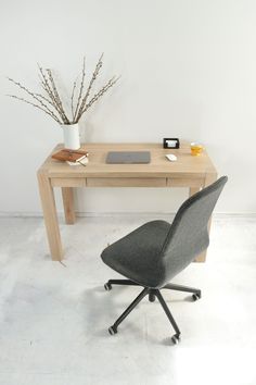 an office desk with a laptop on it and a chair next to it, in front of a white wall