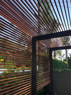 a wooden slatted roof with plants and trees in the back ground below it