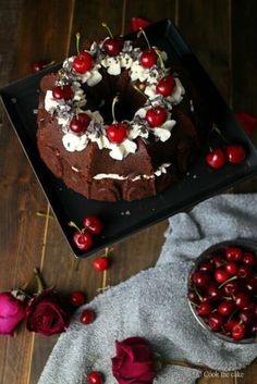 a chocolate cake with cherries and whipped cream is on a black platter next to roses