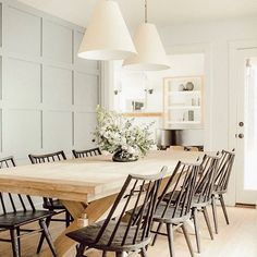 a dining room table surrounded by chairs in front of a white wall with paneling