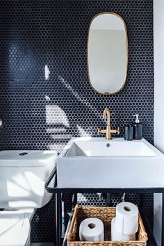 a white sink sitting under a mirror next to a toilet and a basket with rolls of toilet paper