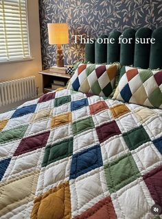 a bed with a colorful quilt on top of it next to a nightstand and lamp