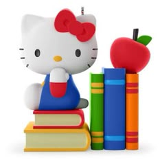 a hello kitty figurine sitting on top of books with an apple and pencil