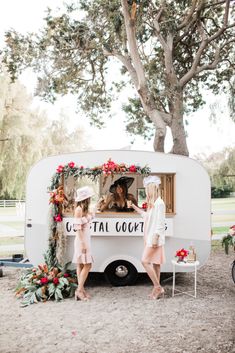 two women standing in front of a food truck with flowers on the side and a sign that says cuco taco