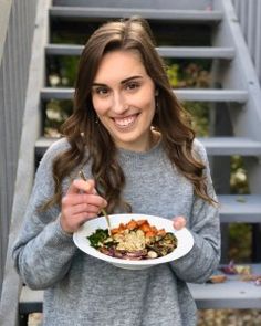 a woman holding a plate of food in front of her face and stairs behind her