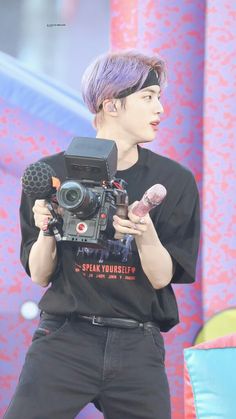 a man with purple hair holding a camera and doughnuts in his right hand