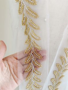 a hand is holding onto some gold and white beaded trimmings on fabric